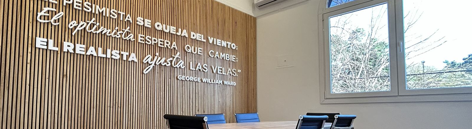 Sala de reuniones con mesa de madera y frase en la pared